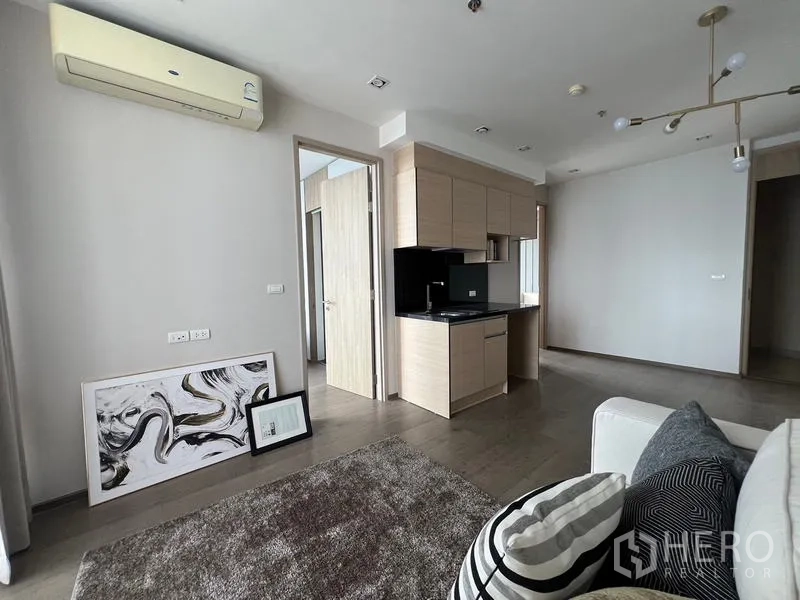 คอนโด ขาย - มุมห้องนั่งเล่นพร้อมพรม โซฟา แอร์ และกรอบภาพพิงผนัง