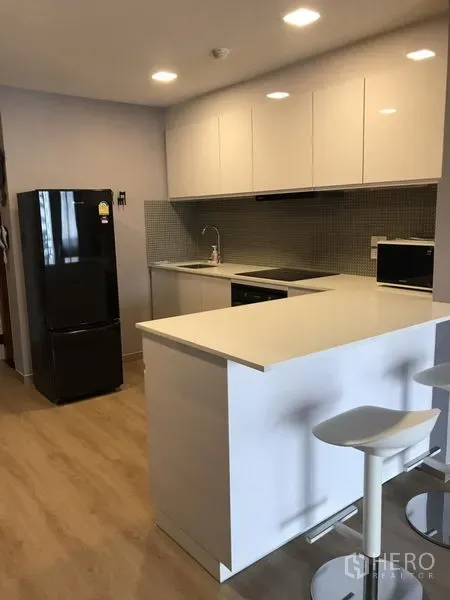 公寓 出租在Bang Rak, Bangkok - 现代白色厨房，带岛台吧台、黑色冰箱、马赛克墙砖与木地板。