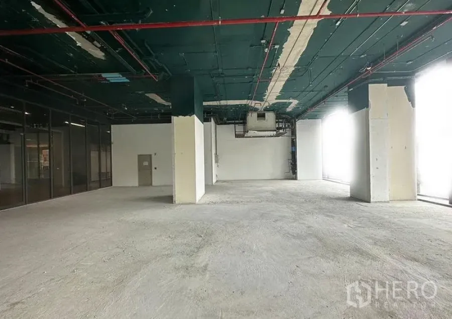 Retail Space for rent in Khlong Toei, Bangkok - Bare-shell retail interior with high exposed ceiling, concrete floor, structural columns, and full-height windows allowing natural light.