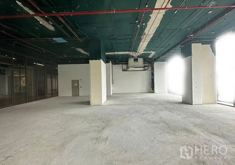 Retail Space for rent in Khlong Toei, Bangkok - Bare-shell retail interior with high exposed ceiling, concrete floor, structural columns, and full-height windows allowing natural light.