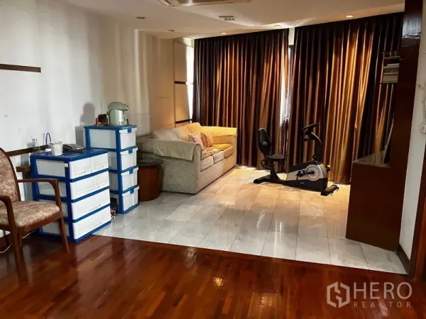 คอนโด ให้เช่าหรือขายในKhlong Toei, Bangkok - มุมนั่งเล่นพร้อมโซฟาและจักรยานออกกำลังกาย บนพื้นกระเบื้องข้างผ้าม่านสูงจรดเพดาน