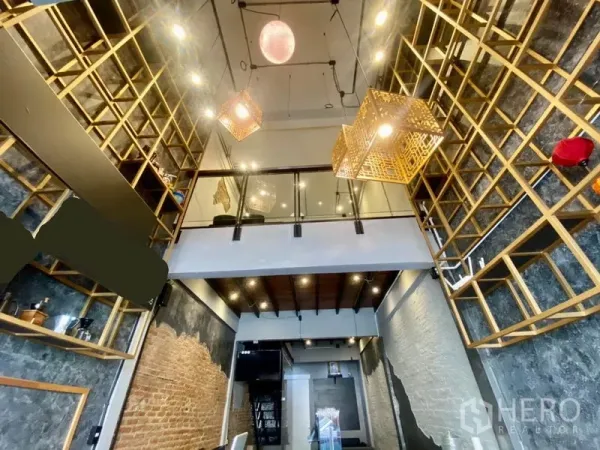 Shophouse for rent in Pathum Wan, Bangkok - Upward view of mezzanine, exposed brick feature walls and geometric gold pendant lights in the shopfront.