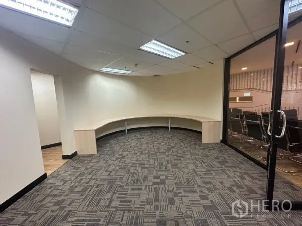 办公空间 出租 - 弧形工作区，配长条内置工作台、地毯地面，并有玻璃门通往会议室。