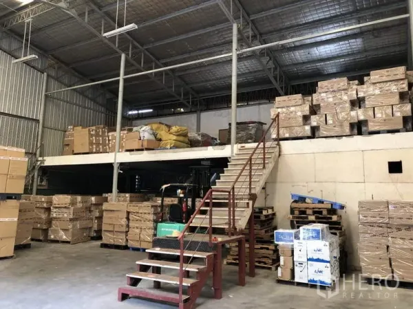 Warehouse for rent in Suan Luang, Bangkok - High-ceiling warehouse interior with mezzanine, stairs, forklift, and palletized boxes.
