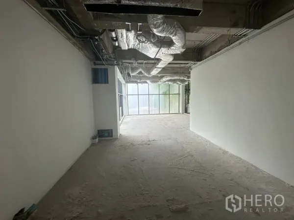 Office Space for rent in Khlong Toei, Bangkok - Long rectangular office bay with frosted glass end wall, raw concrete floor and visible HVAC piping.