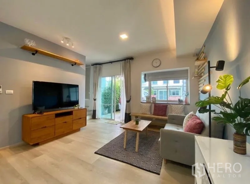 ทาวน์เฮาส์ ให้เช่าในBang Phli, Samut Prakan - มุมนั่งเล่นพร้อมชั้นวางทีวี ประตูกระจกสไลด์ออกสู่เฉลียง และเบาะนั่งริมหน้าต่าง