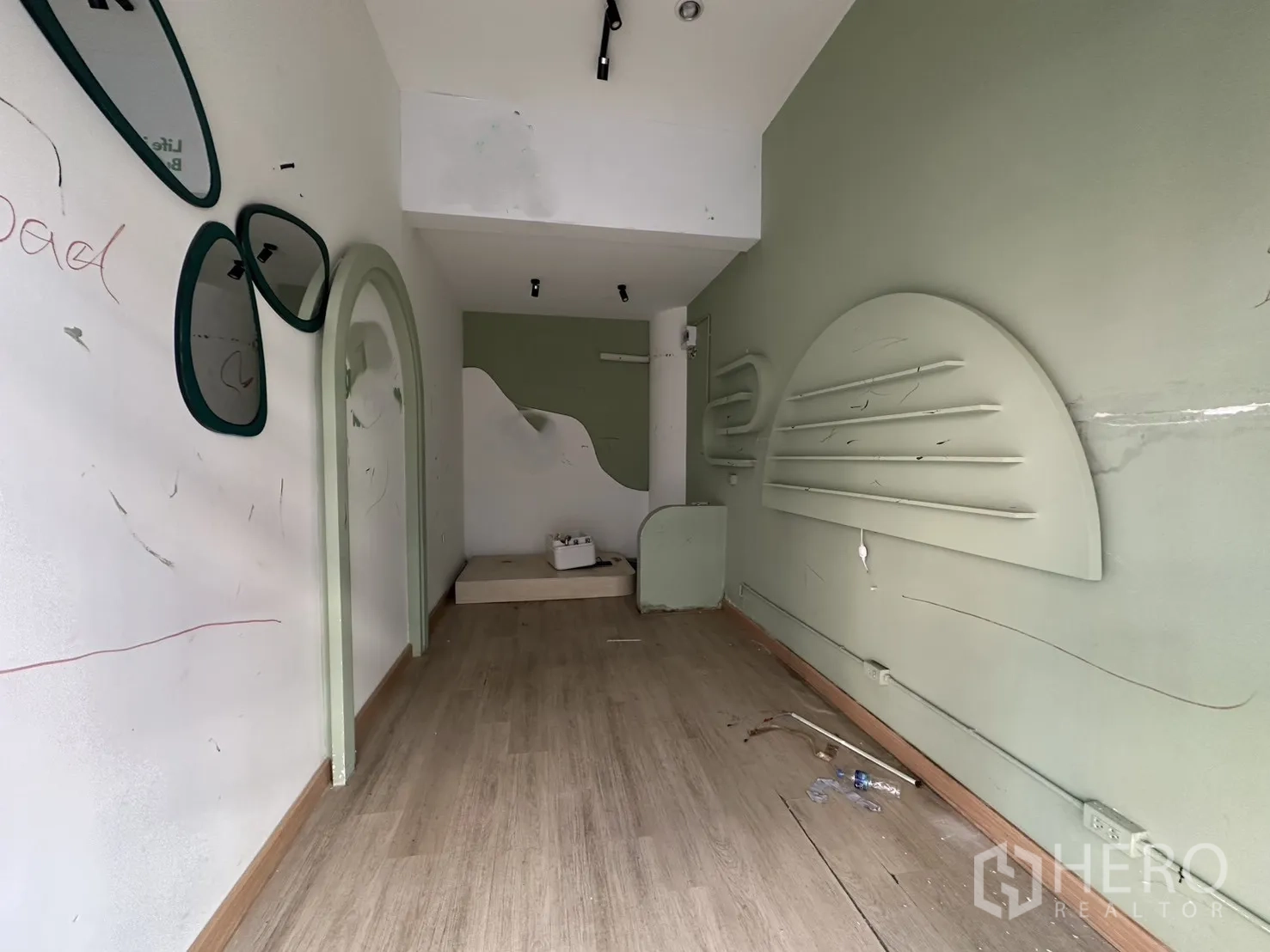 Retail Space for rent in Khlong Toei, Bangkok - Narrow retail interior with light wood floors, sage-green walls, arched niche, mirrors and built-in display shelving.