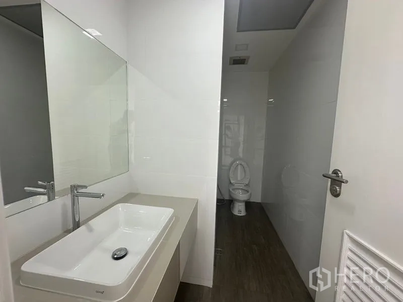 办公空间 出租 - 洁净浴厕空间，宽台面洗手盆、墙面镜与独立马桶区域。