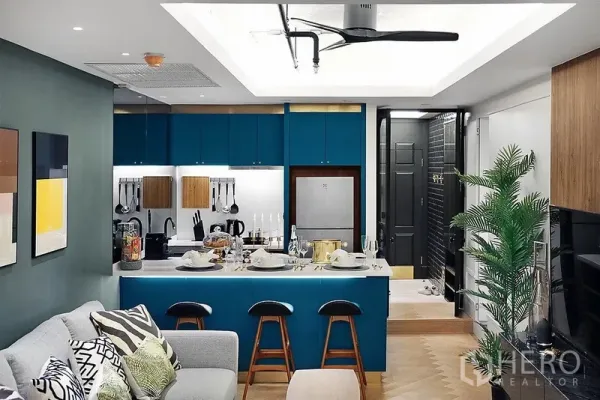 公寓 出租在Bang Rak, Bangkok - 开放式厨房配青绿色橱柜与备餐岛台，连接舒适客厅与吊扇。