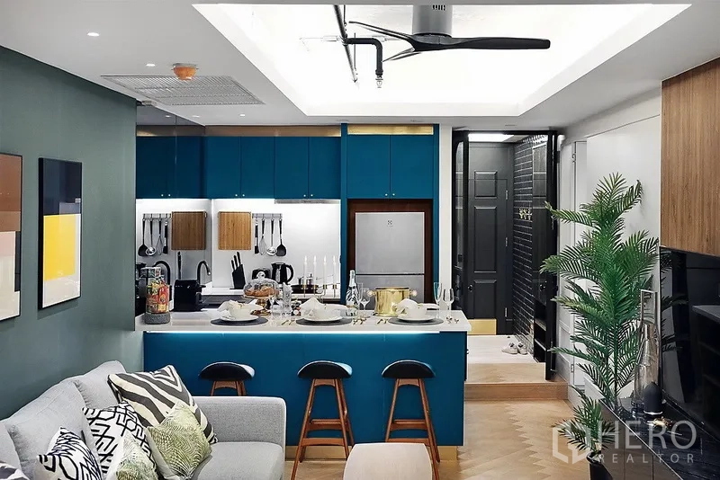 公寓 出租在Bang Rak, Bangkok - 开放式厨房配青绿色橱柜与备餐岛台，连接舒适客厅与吊扇。