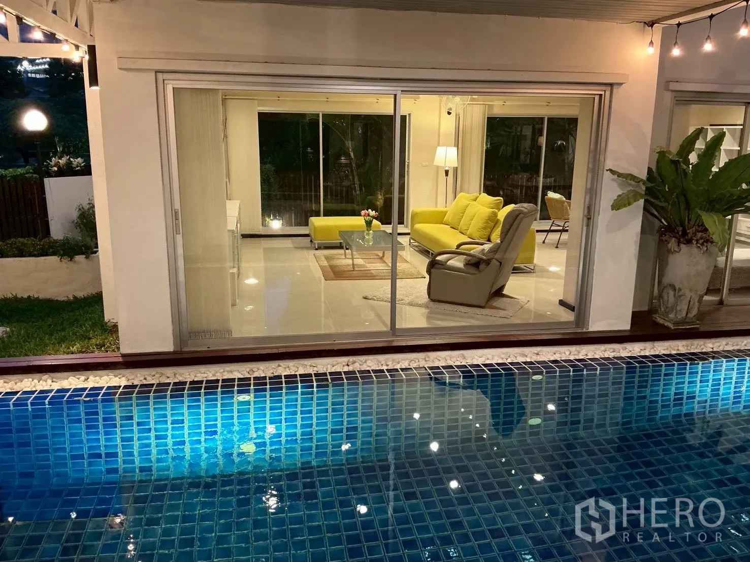 บ้านเดี่ยว for sale in Suan Luang, Bangkok - ยามค่ำเห็นห้องนั่งเล่นโซฟาสีเหลืองจากฝั่งสระว่ายน้ำ
