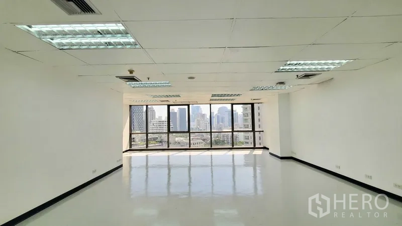 Office Space for rent in Watthana, Bangkok - Bright unfurnished office with large windows, suspended ceiling lighting, and Bangkok skyline views.