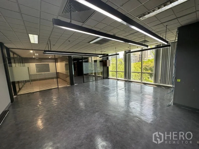 Office Space for rent - Open office zone with glass partitions, hanging linear lights and greenery outside the windows.