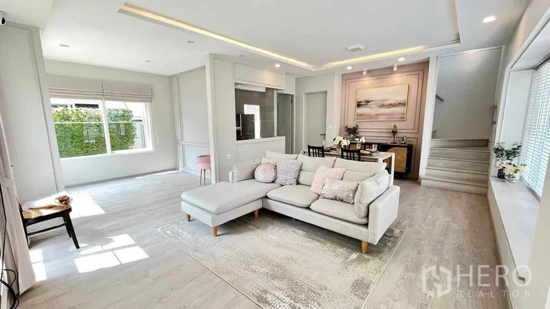 Detached House for rent or sale in Prawet, Bangkok - Spacious living room with L-shaped sofa, large windows and staircase.