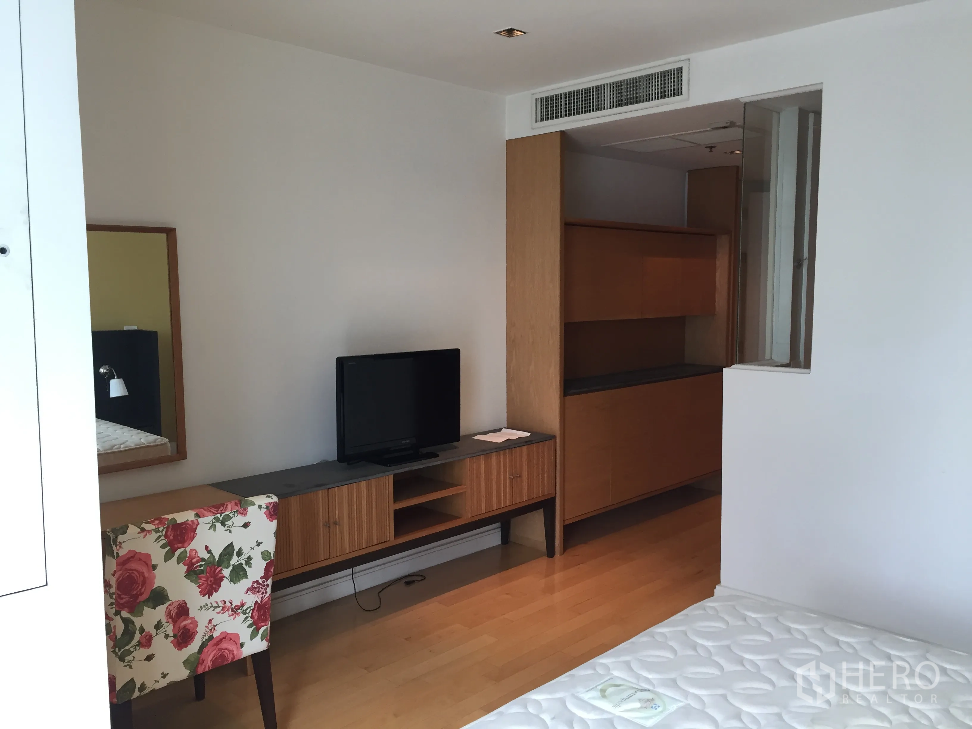 Condominium for rent or sale in Pathum Wan, Bangkok - Bright bedroom corner with TV console, floral accent chair and built-in storage.