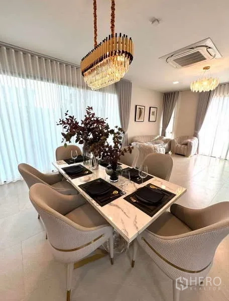 Detached House for rent in Samut Prakan - Dining room with marble table, gold chandelier and sheer curtains.