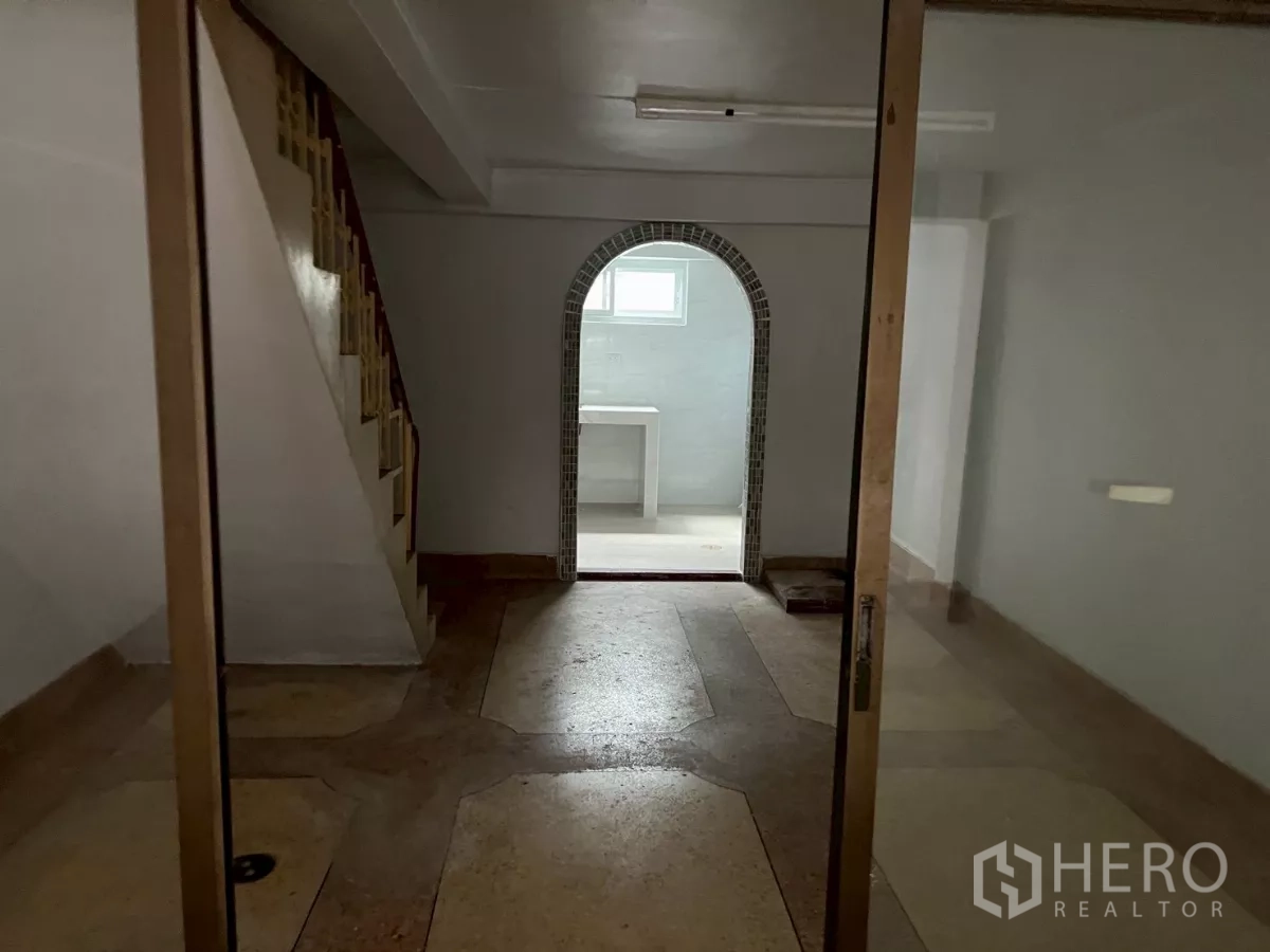 อาคารพาณิชย์ ให้เช่าในKhlong Toei, Bangkok - มุมมองภายในสู่ห้องด้านหลังซุ้มโค้ง พร้อมบันไดและประตูกระจกชั้นล่าง.