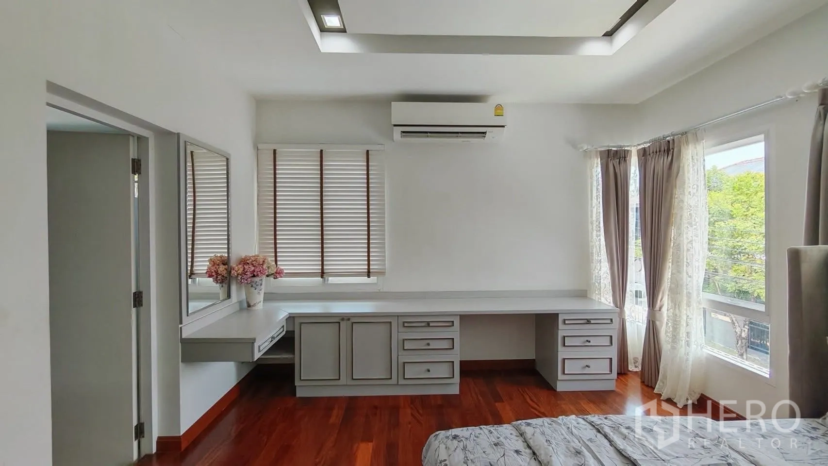 Detached House for rent or sale in Bang Phli, Samut Prakan - Bright bedroom with built-in desk, air conditioner, and large windows with sheer curtains over hardwood floors.