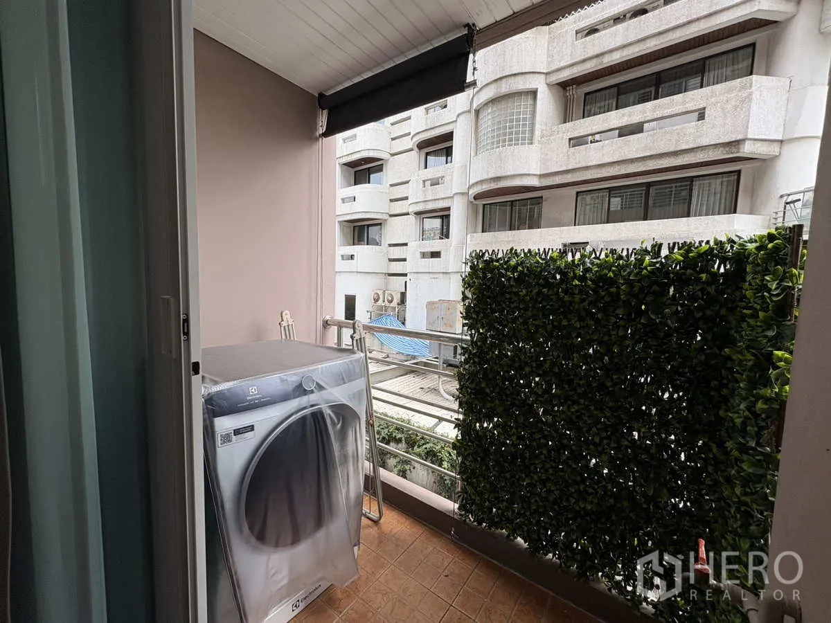 公寓 出租在Khlong Toei, Bangkok - 私密阳台配洗衣机与绿篱，可眺望邻近建筑。