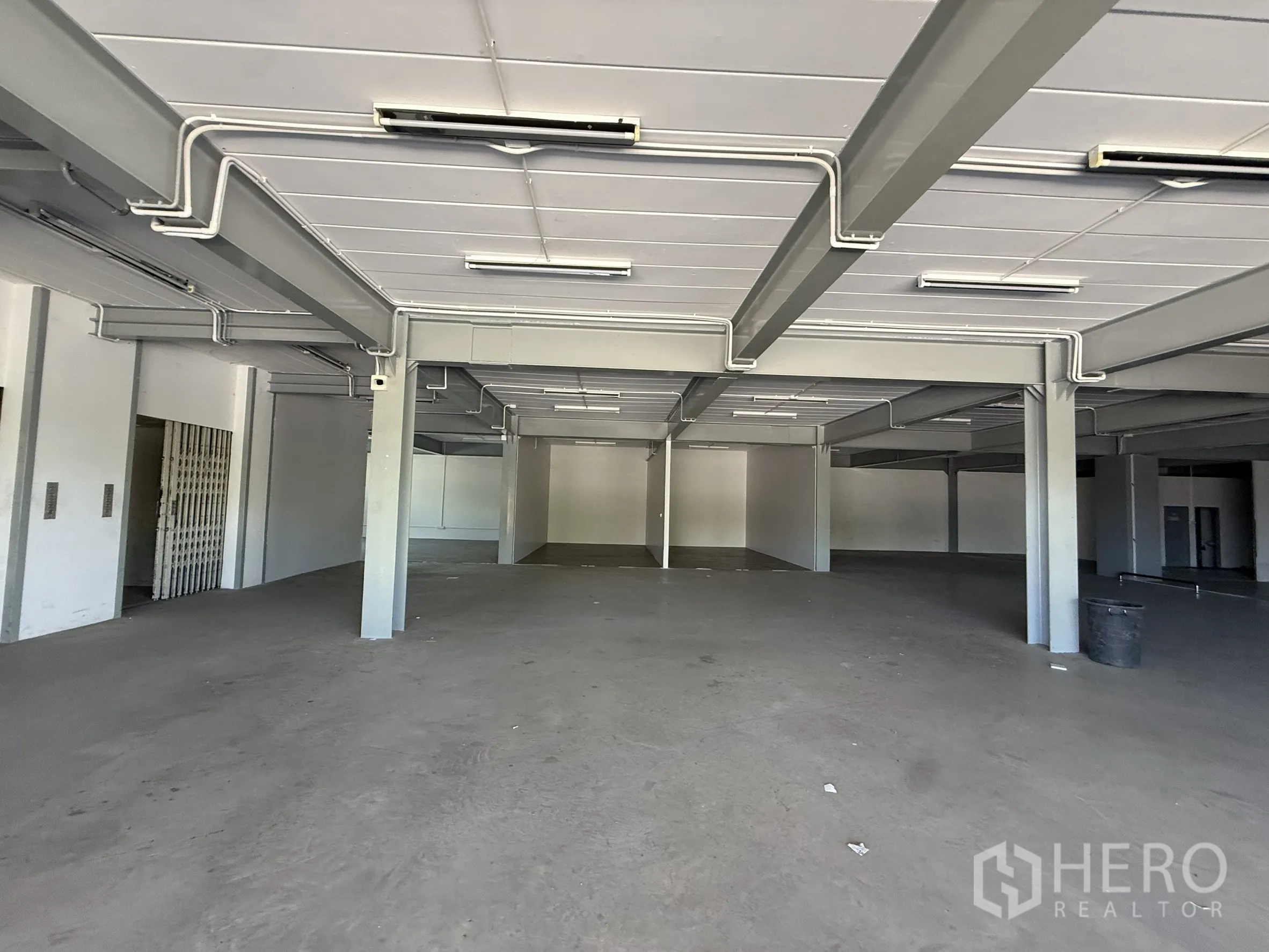 Warehouse for rent in Bueng Kum, Bangkok - Open interior showing steel beams, conduit lighting, and unobstructed floor space.