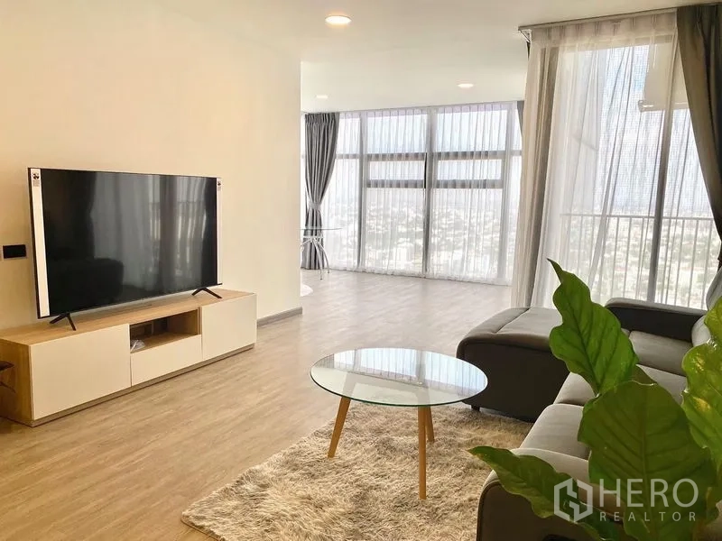 คอนโด ให้เช่า - มุมนั่งเล่นพร้อมทีวีจอใหญ่และวิวเมืองแบบพาโนรามาผ่านกระจกเต็มสูง