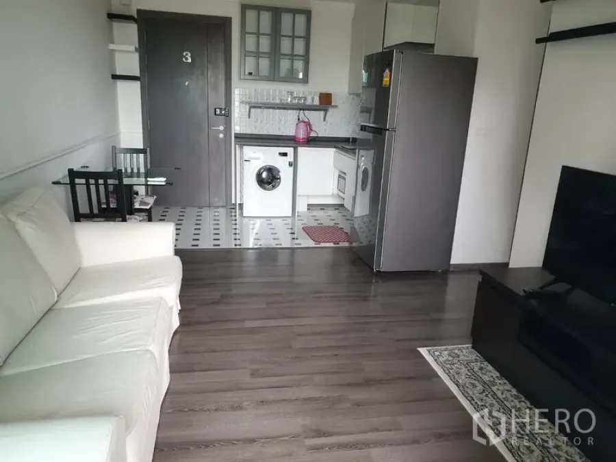 Condominium for rent in Watthana, Bangkok - Open-plan living room with white sofa, TV console, and kitchenette with washing machine.