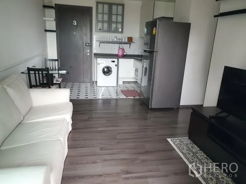 Condominium for rent in Watthana, Bangkok - Open-plan living room with white sofa, TV console, and kitchenette with washing machine.