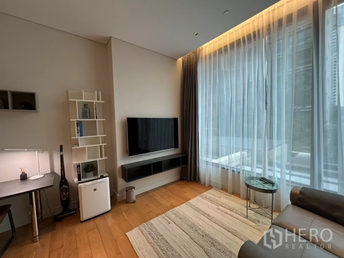 คอนโด ให้เช่าในPathum Wan, Bangkok - ผนังทีวีและโต๊ะทำงานริมผ้าม่านโปร่งของหน้าต่างสูงในห้องนั่งเล่น