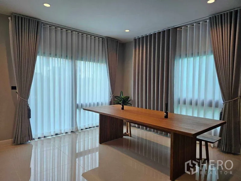 Detached House for rent in Mueang Pathum Thani, Pathum Thani - Dining area with long wooden table by floor-to-ceiling windows