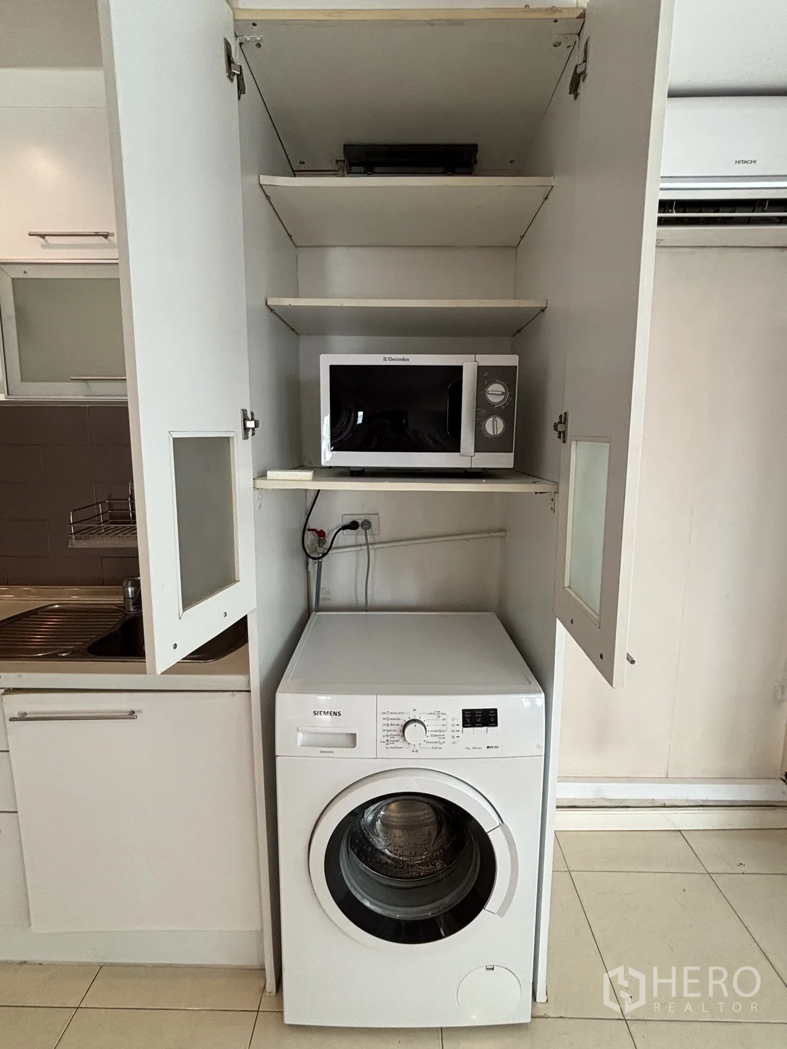 Condominium for rent or sale in Watthana, Bangkok - Kitchen tall cabinet opened to show shelves with a microwave above the washing machine.