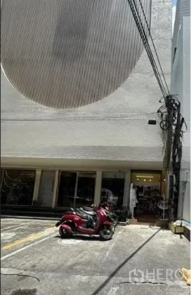 零售空间 出租在Watthana, Bangkok - 建筑前场地，划线停车位与一辆红色踏板车，临近一层商铺。