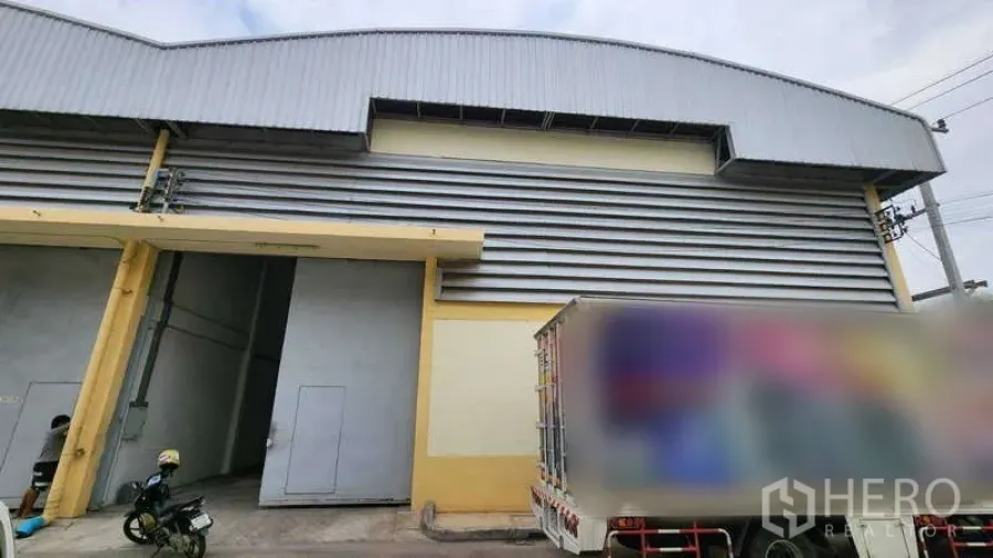 货栈 出租在Ban Phaeo, Samut Sakhon - 仓库外立面，高卷闸门与金属板墙体，设装卸车位，临近Ekachai路