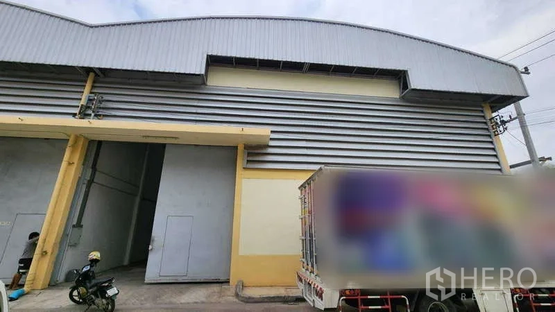 货栈 出租在Ban Phaeo, Samut Sakhon - 仓库外立面，高卷闸门与金属板墙体，设装卸车位，临近Ekachai路