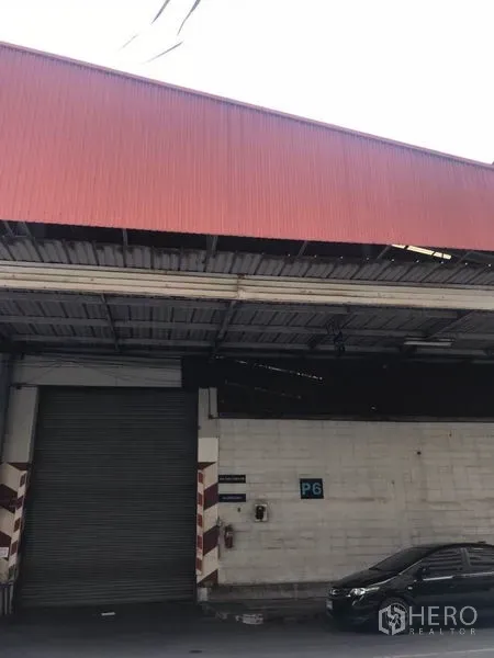 คลังสินค้า ให้เช่าในMueang Samut Prakan, Samut Prakan - ด้านหน้าโกดัง หลังคาเมทัลชีทสีแดง พร้อมประตูม้วนขนาดใหญ่