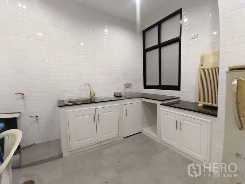 Shophouse for rent or sale in Pom Prap Sattru Phai, Bangkok - Compact white kitchen with subway-tile walls, black countertops, and sink.