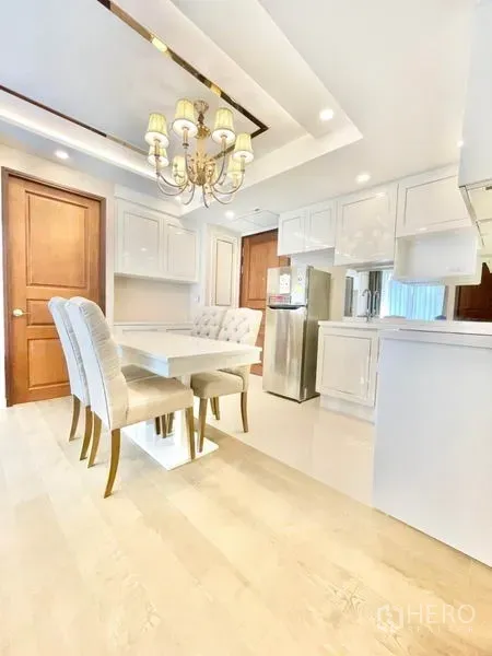 Condominium for sale in Huai Khwang, Bangkok - Open kitchen and dining with white cabinetry, chandelier and full-size fridge.