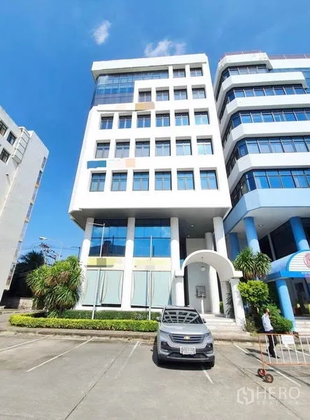 Office Space for rent in Bang Na, Bangkok - Modern mid-rise office building exterior in Bang Na, Bangkok with parking spaces and a landscaped entrance.