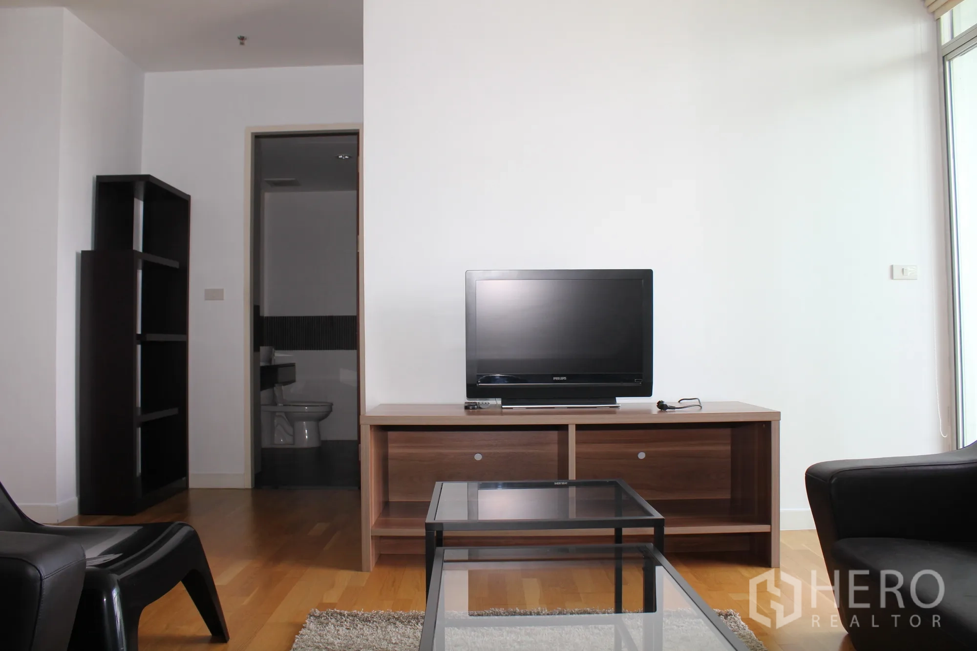 公寓 出租在Sathon, Bangkok - 起居区配电视柜、玻璃茶几，并可见通往浴室的门。