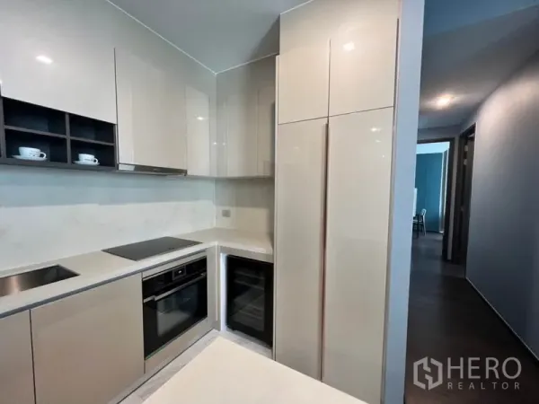 Condominium for rent in Watthana, Bangkok - Modern L-shaped kitchen featuring induction cooktop, built-in oven and wine fridge with sleek cabinets.