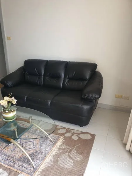 Condominium for rent in Watthana, Bangkok - Black leather sofa and glass coffee table on a rug in the lounge.