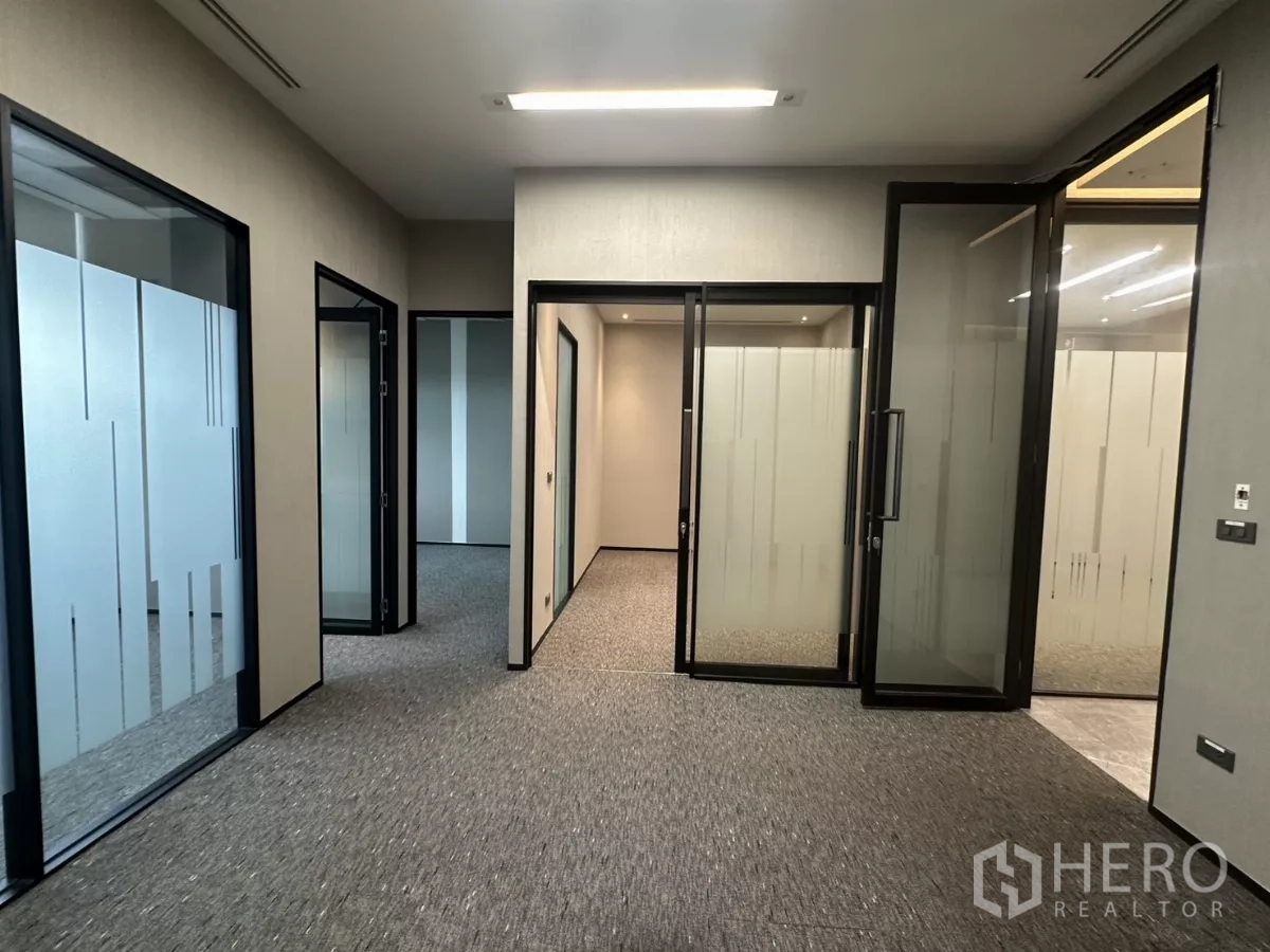 办公空间 出租在Watthana, Bangkok - 铺地毯的走廊，通向带磨砂玻璃门的独立办公室。