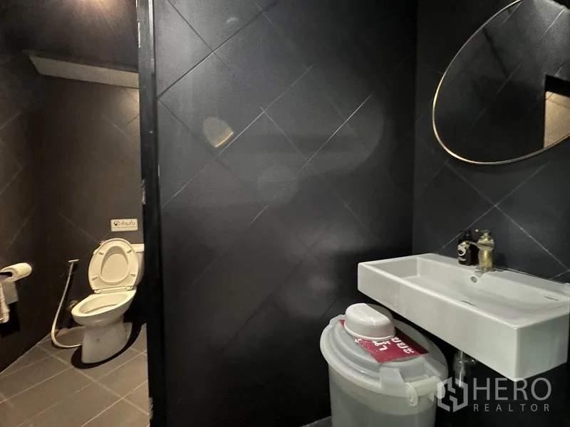 Retail Space for rent in Phra Khanong, Bangkok - Restroom with white sink and round mirror next to toilet cubicle.