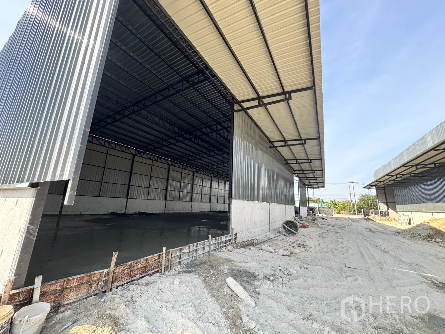 Warehouse for rent in Lam Luk Ka, Pathum Thani - Under‑construction warehouse with wide canopy roof and a large opening for trucks.