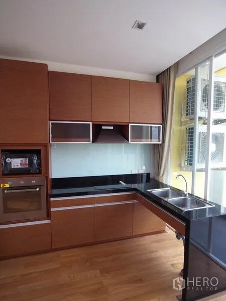 公寓 出租在Chatuchak, Bangkok - L形现代厨房，木质橱柜、黑色台面与双槽水槽。