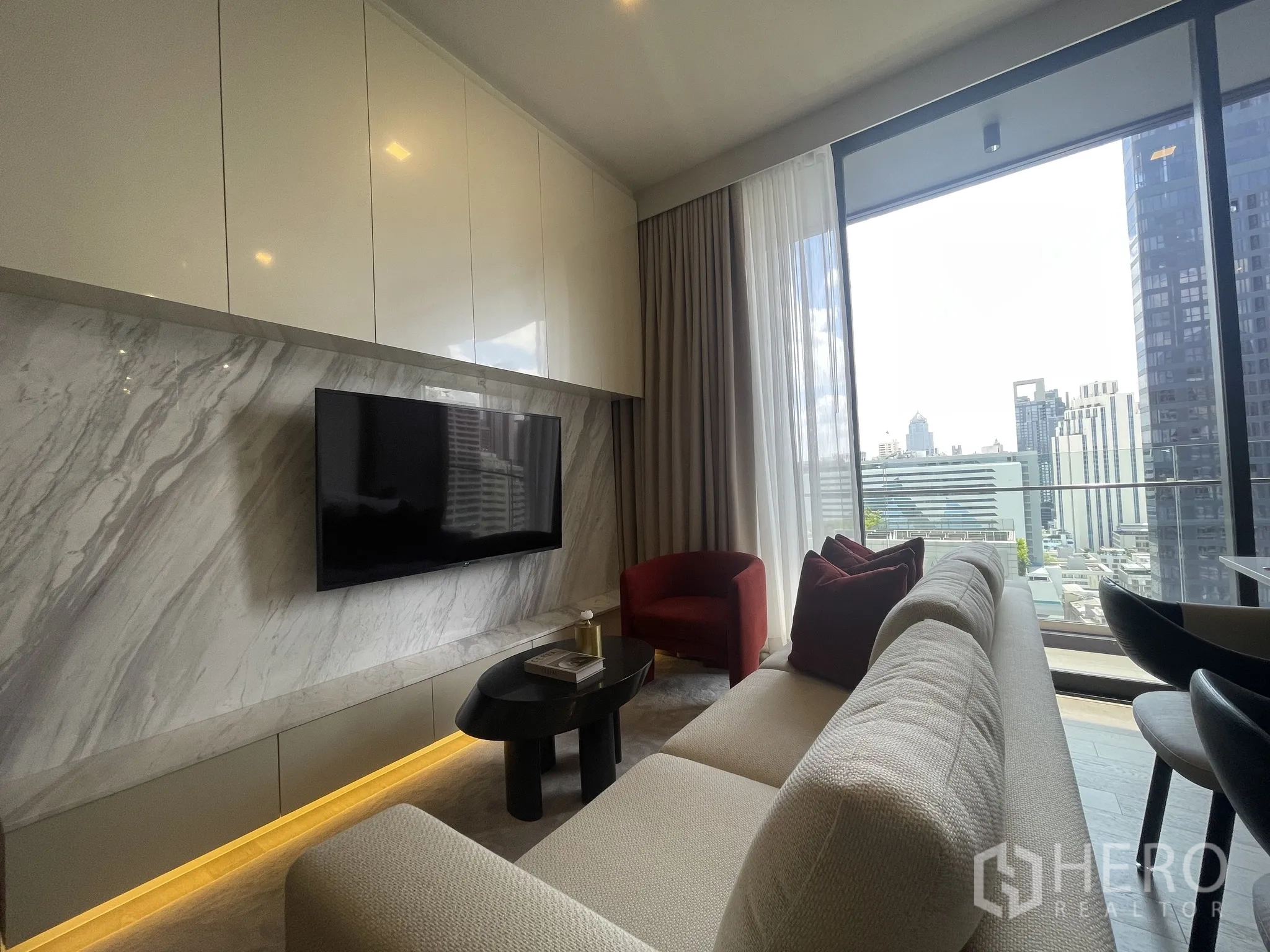 Condominium for rent in Watthana, Bangkok - Living room with marble feature wall, mounted TV, and floor-to-ceiling windows.