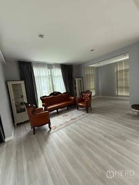 Detached House for rent or sale in Bang Bua Thong, Nonthaburi - Bright living room with large windows, curtains, and classic leather sofa set on a rug.