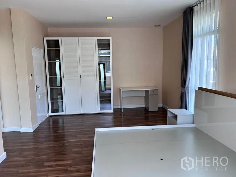 Detached House for rent or sale in Prawet, Bangkok - Large bedroom with wardrobe, desk, and wood flooring.