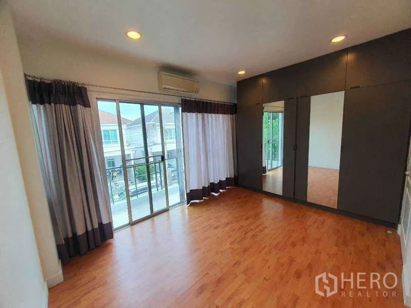 Detached House for rent in Saphan Sung, Bangkok - Bedroom with floor‑to‑ceiling wardrobes, wood floors and sliding doors to a balcony.