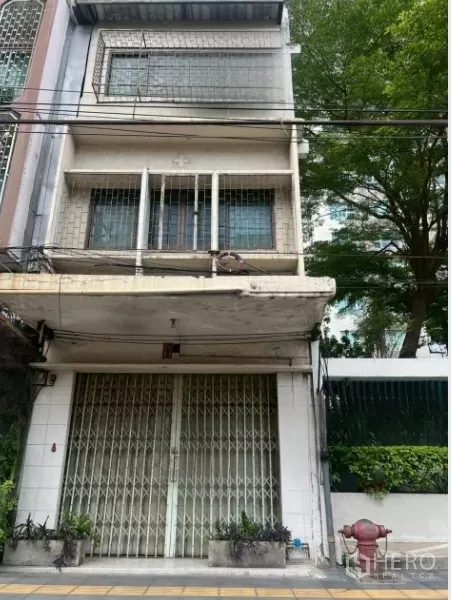 อาคารพาณิชย์ ขาย - อาคารพาณิชย์หลายชั้น หน้ากว้างพร้อมประตูเหล็กพับ ระเบียงเล็ก และกระถางต้นไม้ริมทางเท้า ย่านคลองเตย กรุงเทพฯ