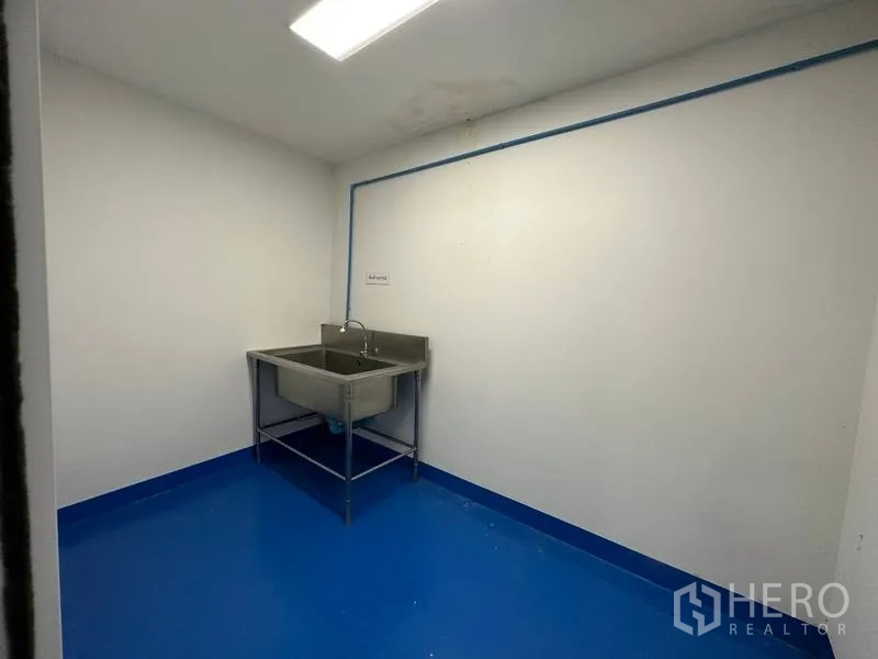 Warehouse for rent in Pak Kret, Nonthaburi - Wash area with a stainless double sink and visible blue service piping.